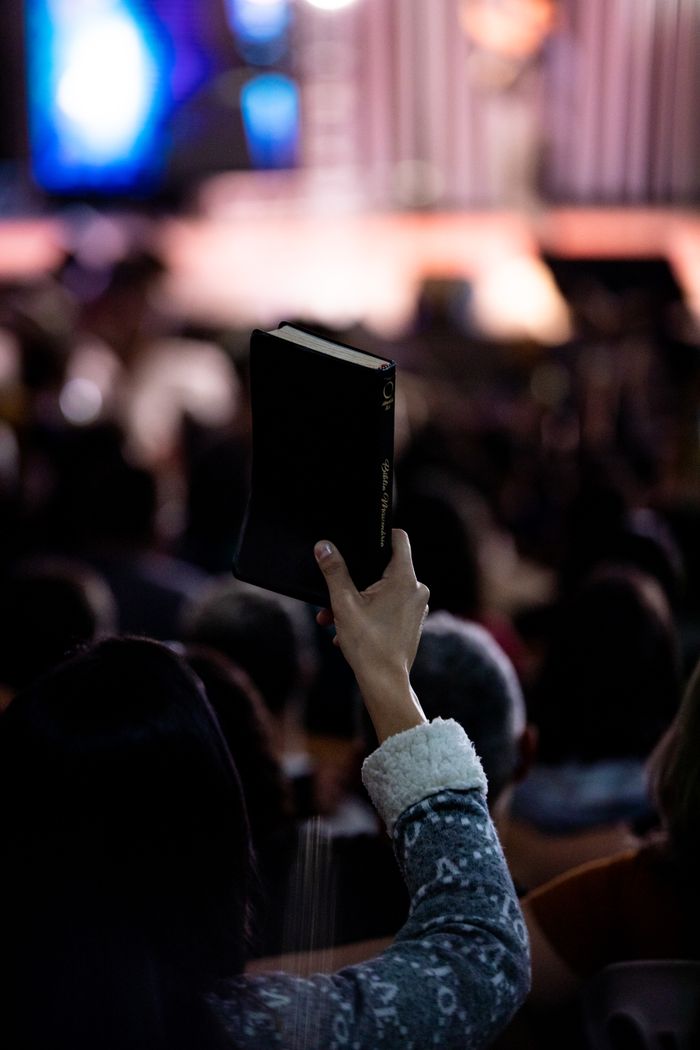 Services A person holds up a Bible during an indoor religious gathering, highlighting faith.