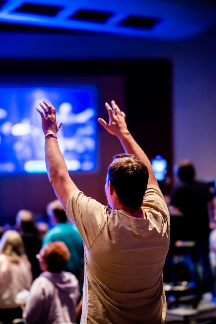 Home A man raises his hands in worship during an indoor religious gathering.