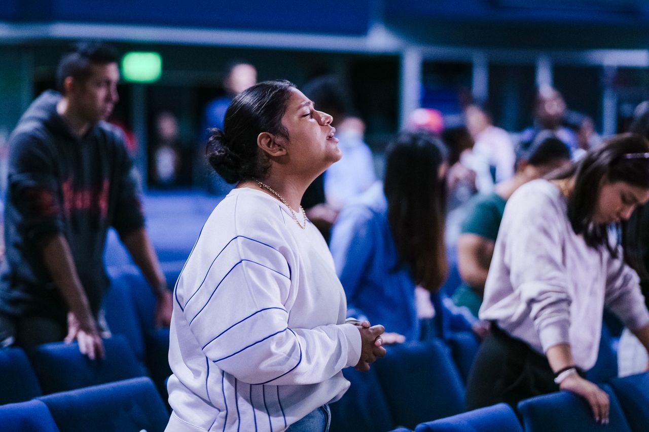 Services A diverse group of adults immersed in prayer inside a serene religious setting.