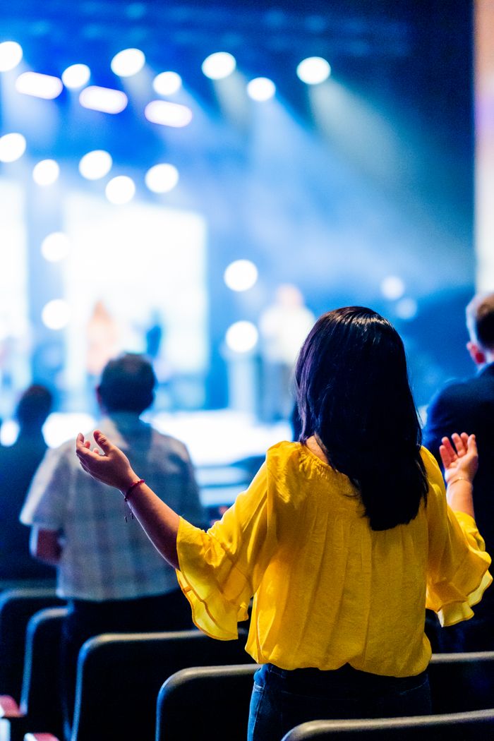 Mastering the First Impression: Your intriguing post title goes here A woman in a yellow blouse with hands raised at a lively concert event indoors.
