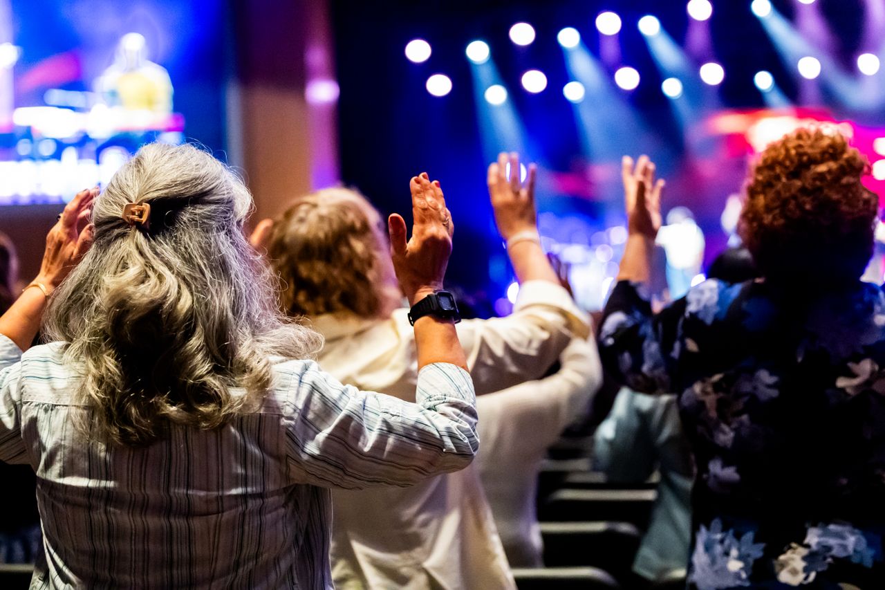 Home A group of people with raised hands attending a lively worship service inside a church.
